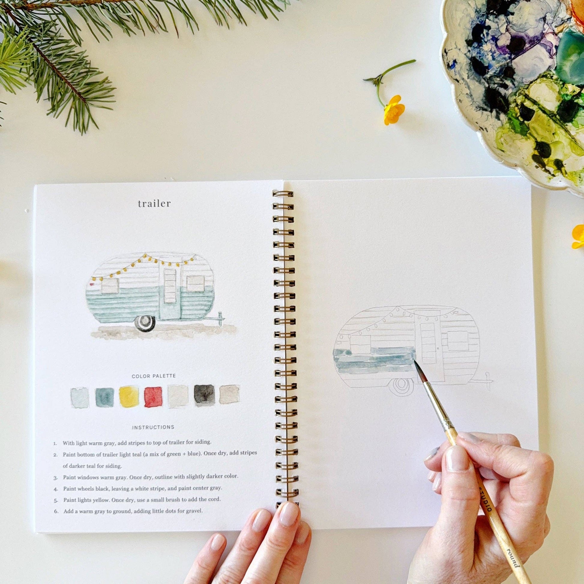 Person painting a watercolor illustration of a camper in a art journal.