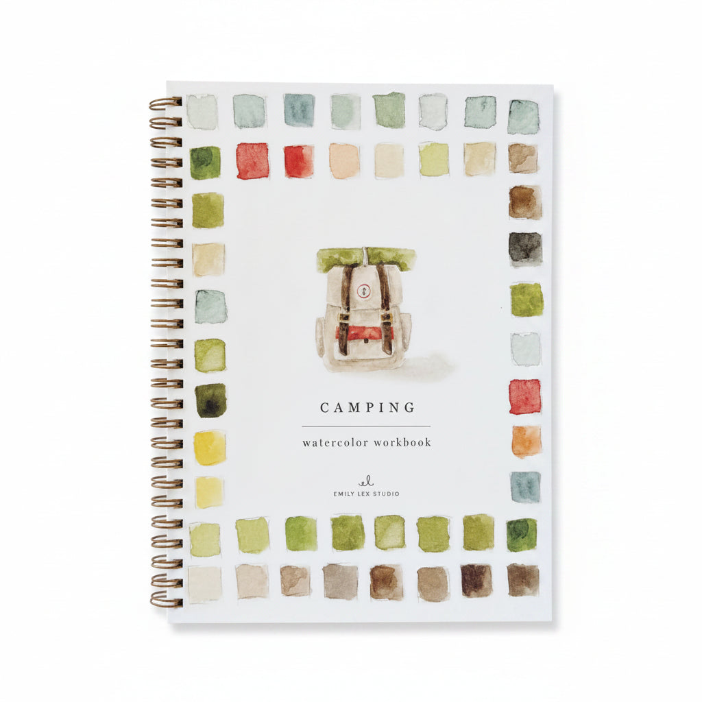 Camping watercolor workbook with color swatches on a white surface with a pen and natural elements.