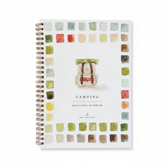 Camping watercolor workbook with color swatches on a white surface with a pen and natural elements.