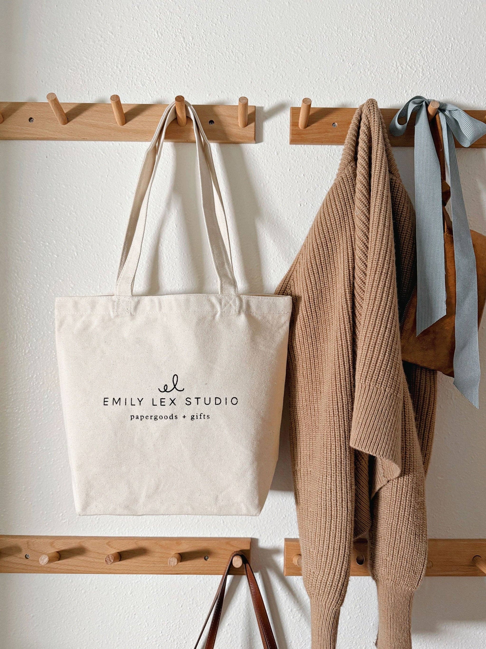 Tote bag with 'Emily Lex Studio' branding hanging on a wooden coat rack.