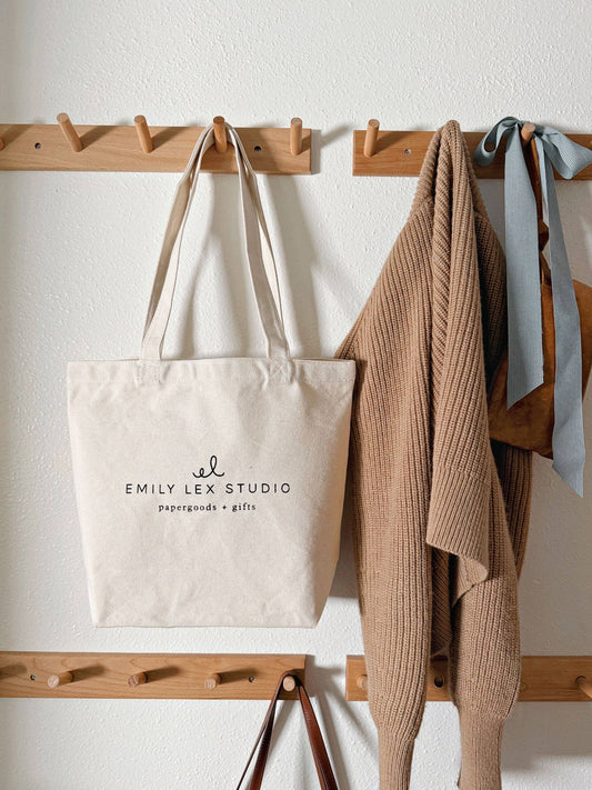 Tote bag with 'Emily Lex Studio' branding hanging on a wooden coat rack.